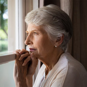 Elderly woman staring out through dreary window