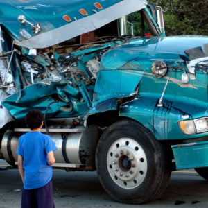 young boy looks at the aftermath of a semi-truck crash